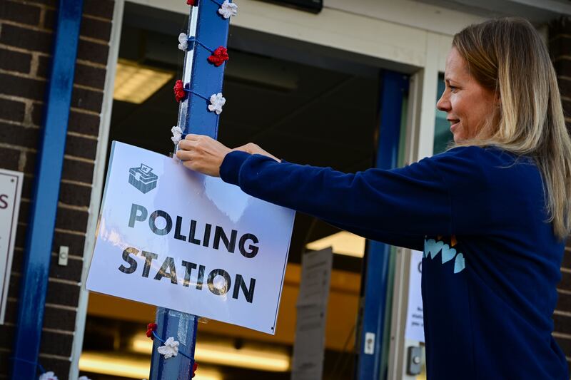 A woman attaches a polling station sign outside Honiton Library in England. The Tiverton and Honiton constituency by-election is being held after Conservative MP Neil Parish resigned. Getty Images
