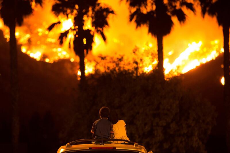 King Bass, 6, left, sits and watches the Holy Fire burn from on top of his parents' car as his sister Princess, 5, rests her head on his shoulder Thursday night, Aug. 9, 2018 in Lake Elsinore, Calif.  More than a thousand firefighters battled to keep a raging Southern California forest fire from reaching foothill neighborhoods Friday before the expected return of blustery winds that drove the flames to new ferocity a day earlier. (AP Photo/Patrick Record)