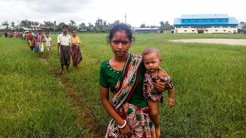 A woman holds a child in her arms as she arrives at the Yathae Taung township in Rakhine State in Myanmar after fleeing from violence in their village on August 26, 2017. 
Terrified civilians tried to flee remote villages in Myanmar's northern Rakhine State for Bangladesh on August 26 afternoon, as clashes which have killed scores continued between suspected Rohingya militants and Myanmar security forces. / AFP PHOTO / Wai Moe