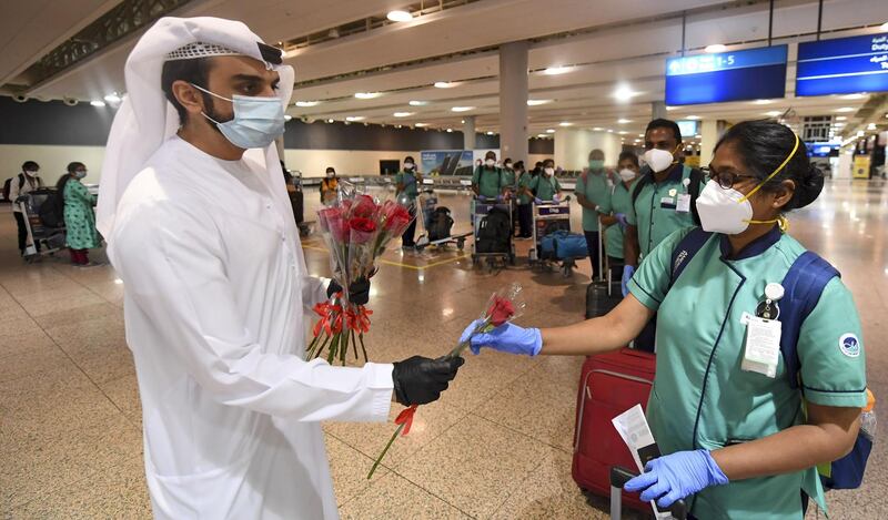 An Emirati official presents a rose to an Indian health worker, part of an 80 person medical team, upon their arrival at Dubai International Airport on May 9, 2020.  / AFP / Karim SAHIB
