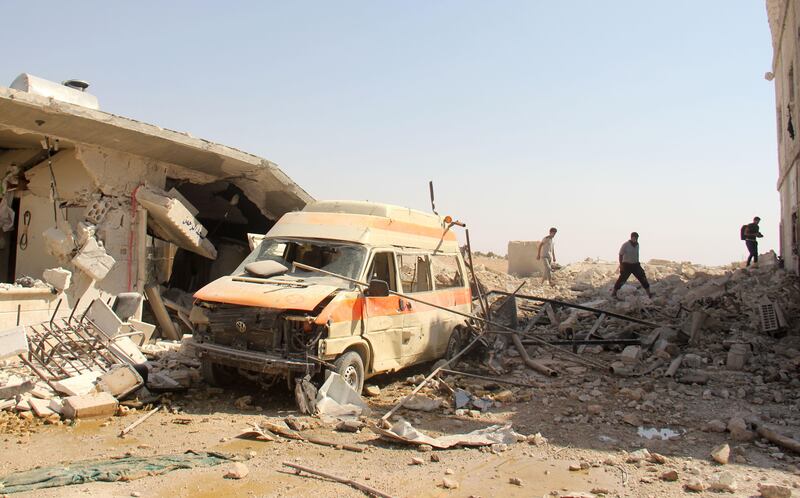 A picture taken on September 19, 2017 shows people walking through rubble and debris past a damaged ambulance following a reported air strike by Syrian government forces in the village of Al-Tahh, in the northwestern Idlib province. / AFP PHOTO / Omar haj kadour