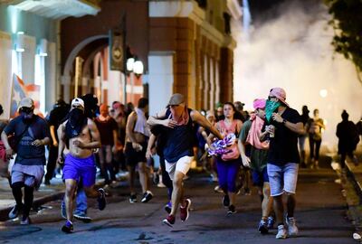 Demonstrators affected by tear gas thrown by the police run during clashes in San Juan, Puerto Rico, Monday, July 22, 2019.  Protesters are demanding Rossello step down following the leak of an offensive, obscenity-laden online chat between him and his advisers that triggered the crisis.  (AP Photo/Carlos Giusti)