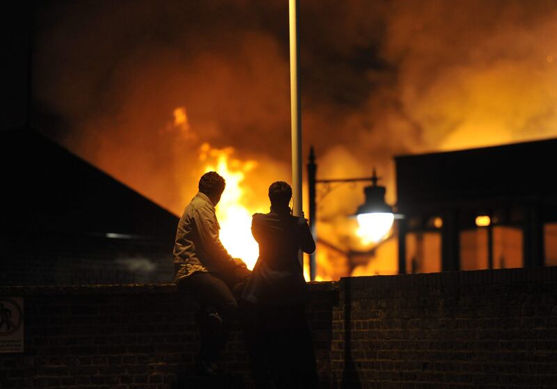epa02858604 A young couple watches the flames of a burning block of buildings from a railway bridge as riots break out in North London's Tottenham, Britain, early 07 August 2011. Angry locals set houses, police cars and a bus alight in reaction to a fatal shooting incident in which a policeman was injured on 04 August and a local 29-year-old man named as Mark Duggan allegedly killed by armed officers.  EPA/DANIEL DEME *** Local Caption ***  02858604.jpg