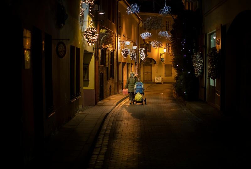 A woman with a baby stroller wearing a face mask to prevent the spread of coronavirus, walks an empty Old Town in Vilnius, Lithuania. Lithuania tightens lockdown, to close shops, restrict movement as of Wednesday. The majority of shops, with the exception of those selling food, closed in Lithuania as of Wednesday as the country is tightening the existing lockdown. AP Photo