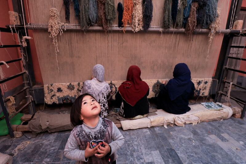 Five-year-old Fatima plays as women weave a carpet in a home workshop in Peshawar, Pakistan. Reuters