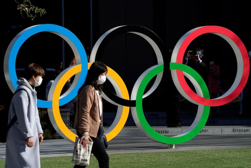 Women wearing protective face masks walk past the Olympic rings in front of the Japan Olympics Museum, a day after the announcement of the games' postponement to 2021. Reuters