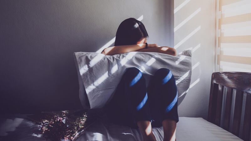 Asian women are sitting hugging their knees in bed. Feeling sad, disappointed in love In the dark bedroom and sunlight from the window through the blinds.Vintage tone. Getty Images