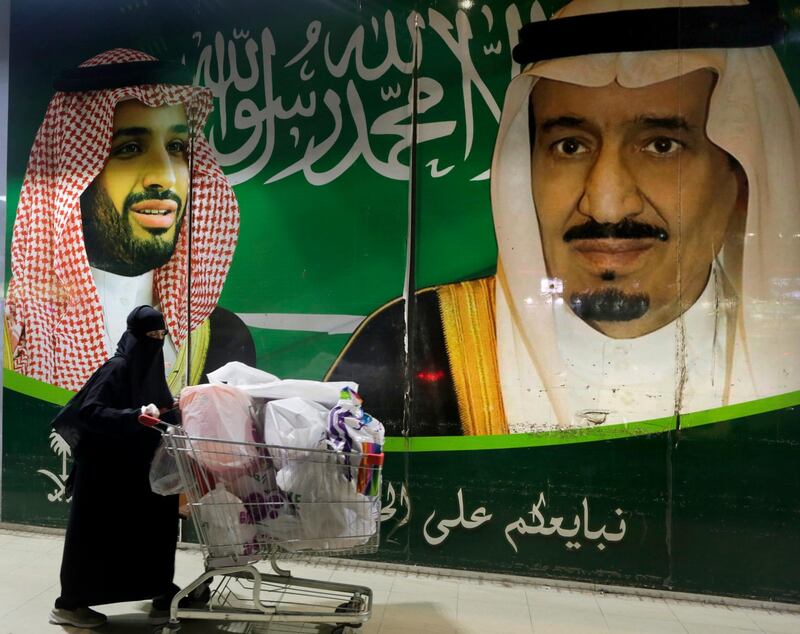 A Saudi woman pushes her shopping cart outside a supermarket a day before the expected increase of VAT from 5% to 15%, in Jiddah, Saudi Arabia. At background a banner showing Saudi King Salman, right, and his Crown Prince Mohammed bin Salman with Arabic reads, "We pledge you to love and loyalty". AP Photo