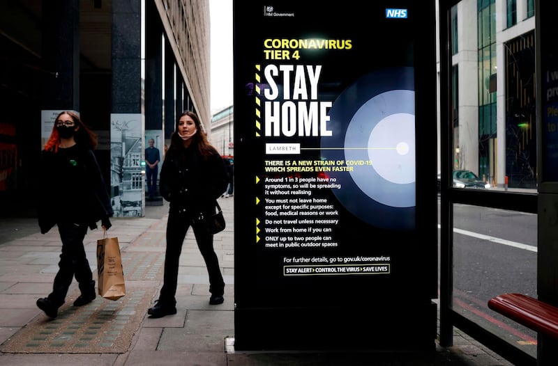 People, some wearing a mask because of the coronavirus pandemic, walk past a bus stop with a government message urging people to stay home in London. AFP