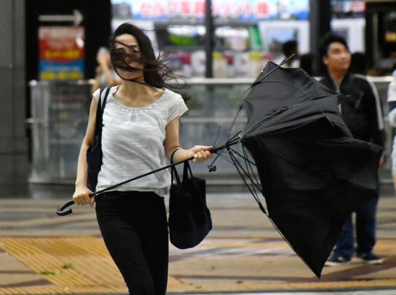 A woman holds a broken umbrella as a powerful typhoon hits Osaka, western Japan. Kyodo News via AP