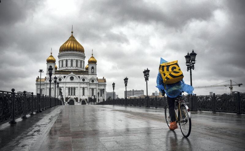 A food delivery courier rides in front of Christ-the-Savior cathedral in central, the main Russian Orthodox church in central Moscow, on June 2, 2020, amid the outbreak of COVID-19, caused by the novel coronavirus, as Moscow authorities started opening churches, mosques and synagogues. (Photo by Alexander NEMENOV / AFP)