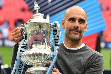 Manchester City's Spanish manager Pep Guardiola holds the winner's trophy as the players celebrate victory after the English FA Cup final football match between Manchester City and Watford at Wembley Stadium in London, on May 18, 2019. - Manchester City beat Watford 6-0 at Wembley to claim the FA Cup. (Photo by Glyn KIRK / AFP) / NOT FOR MARKETING OR ADVERTISING USE / RESTRICTED TO EDITORIAL USE