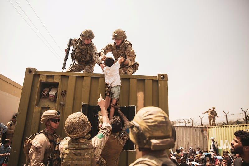UK coalition forces, Turkish coalition forces, and US  Marines assist a child during an evacuation at Hamid Karzai International Airport, Kabul, in August. Reuters