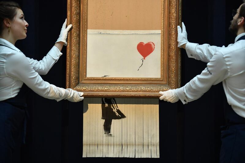 Sotheby's employees pose with the newly completed work by artist Banksy entitled "Love is in the Bin", a work that was created when the painting "Girl with Balloon" was passed through a shredder in a surprise intervention by the artist, at Sotheby's auction house in London on October 12, 2018, following the work's sale. - The buyer of a work by street artist Banksy that was partially destroyed moments after it sold has gone through with the purchase, Sotheby's auction house said on October 11, 2018. The painting "Girl with Balloon" was passed through a shredder hidden in the frame just after it went under the hammer last week for £1,042,000 ($1.4 million, 1.2 million euros). The modified version has now been certified by Banksy's authentication body Pest Control as a new piece of work in its own right, entitled "Love is in the Bin". (Photo by Ben STANSALL / AFP) / RESTRICTED TO EDITORIAL USE - MANDATORY MENTION OF THE ARTIST UPON PUBLICATION - TO ILLUSTRATE THE EVENT AS SPECIFIED IN THE CAPTION