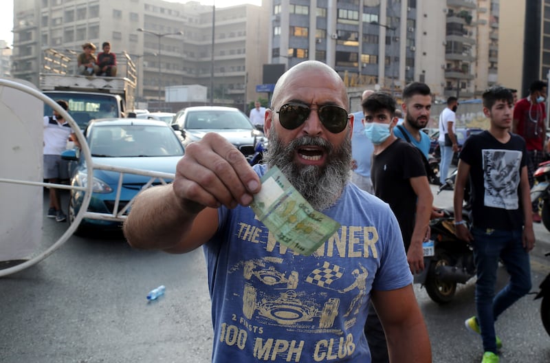 A man gestures with a currency note as Lebanese protesters block the roads with garbage bins and burning tires during protests after Saad Hariri abandoned efforts to form a new government, in Beirut, Lebanon, July 15. EPA