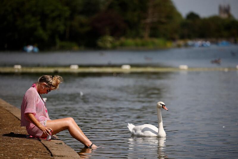 A woman dips her feet into the Serpentine lake in the sunshine in Hyde Park, London. AFP