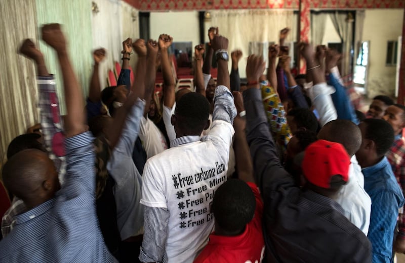 Members of the Kinshasa cell of Filimbi, a pro-democracy group whose name means "whistle" in Swahili, conclude their secret meeting with a cheer in Kinshasa, DRC, Aug. 14, 2018. Filimbi members had just spent the day in court, supporting their imprisoned colleagues, whose names are on the back of the white t-shirt worn by the activist in the middle of this image. After languishing nearly nine months in jail while they awaited a verdict, four of Filimbi's activists were recently convicted of ��disturbing the public order�� and ��insulting the head of state�� and sentenced to one year in prison.