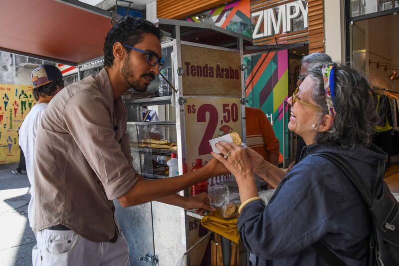 Egyptian immigrant Mohamed Ali Abdelmoatty Kenawy, who was attacked three weeks ago by four men screaming "Go back to your country!", attends to a customer at his food stand in the Copacabana neighborhood in Rio de Janeiro on August 24, 2017.
Mohamed Ali Abdelmoatty Kenawy, who has lived in Rio de Janeiro, Brazil since 2014 and sells Arab food on the street, was the victim of a recent hate crime, and the incident was filmed and posted on the social networks and went viral in Brazil. / AFP PHOTO / Apu Gomes