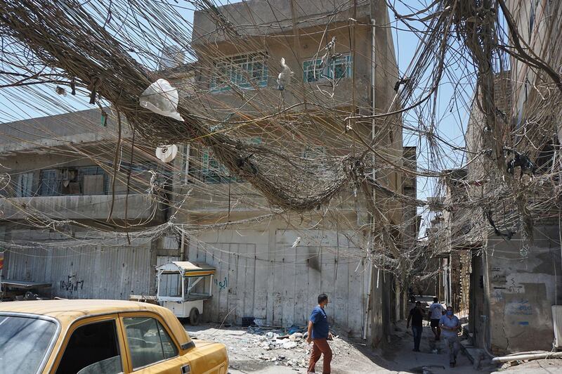 Iraqis walk beneath a web of electric wires in the Syed Sultan Ali area of the capital Baghdad, on July 13, 2020, used to draw electricity from private generators due to an unreliable national electricity supply amid high temperatures. / AFP / SABAH ARAR
