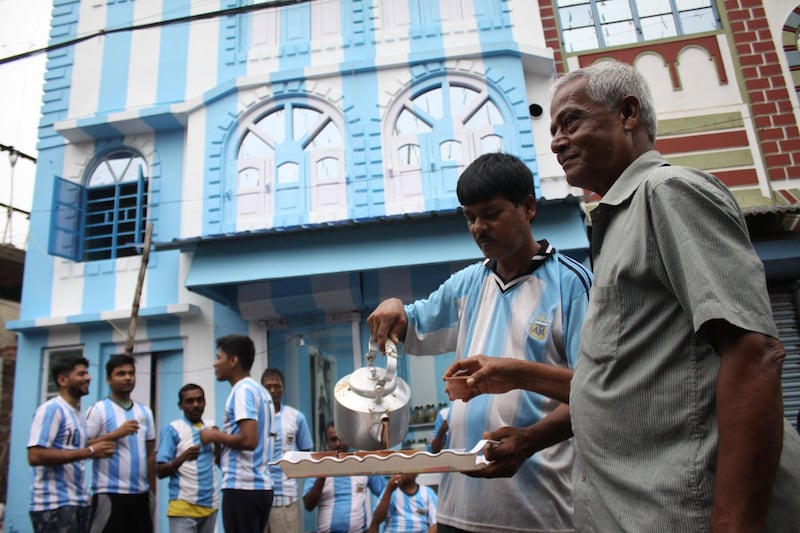 Shib Shankar Patra (2R), football fan of Argentina team, serves tea to fans and customers in front of his apartment painted in blue-and-white, ahead of the upcoming 2018 World Cup, on June 11, 2018. A die-hard Argentina fan in India has painted his house in the team's blue and white colours ahead of the World Cup, saying his love for Lionel Messi's men knows no bounds. Kolkata resident Shib Shankar Patra's passion for Argentina began during the 1986 World Cup when Diego Maradona helped the team win the coveted trophy. / AFP / -
