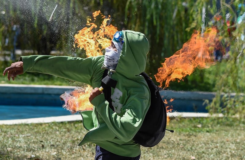 TOPSHOT - A demonstrator throws a Molotov cocktail at riot police during clashes in Caracas on January 22, 2018 which erupted during a protest to condemn the death of dissident former police officer Oscar Perez - gunned down in a bloody police operation on February 16. 
Perez, whose body was buried by the government on January 21 against his family's wishes, was Venezuela's most wanted man since June when he flew a stolen police helicopter over Caracas dropping grenades on the Supreme Court and opening fire on the Interior Ministry.  / AFP PHOTO / Juan BARRETO