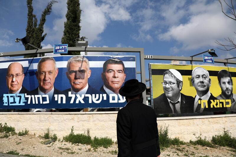 An orthodox Jewish man looks on Blue and White party election campaign poster depicting it's leaders Benny Gantz, Yair Lapid, Moshe Yaalon and Gaby Ashkenazi as well as Israeli Prime Minister Benjamin Netanyahu with members of Israel's far-right political party, Jewish Power, hanging in Jerusalem March 27, 2019. Picture taken March 27, 2019. REUTERS/Ammar Awad