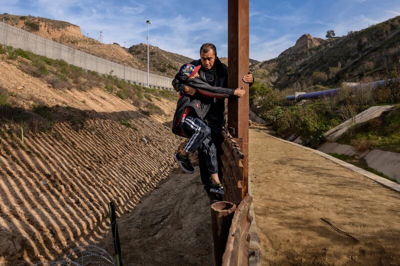 A Honduran migrant grabs his son as they climb the US border fence before jumping across to San Diego from Tijuana, Mexico. AP