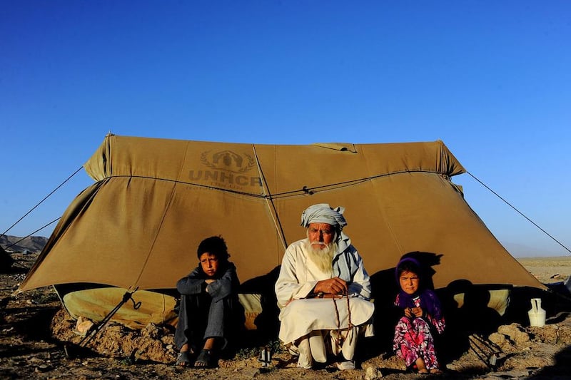 Internally displaced Afghan children sit with an elderly man outside a tent on the outskirts of Herat, Afghanistan.  Aref Karimi / AFP