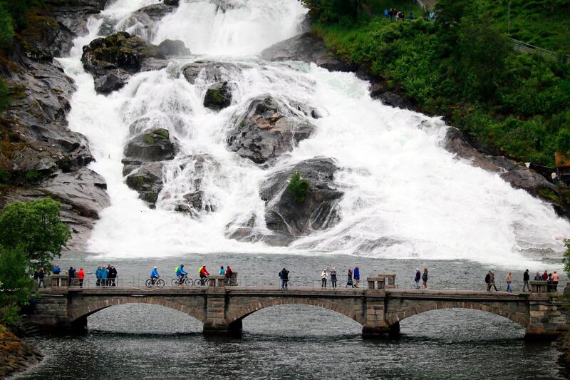 Photo shows people on a bridge at the foot of a waterfall in the town of Hellesylt, Norway. AP