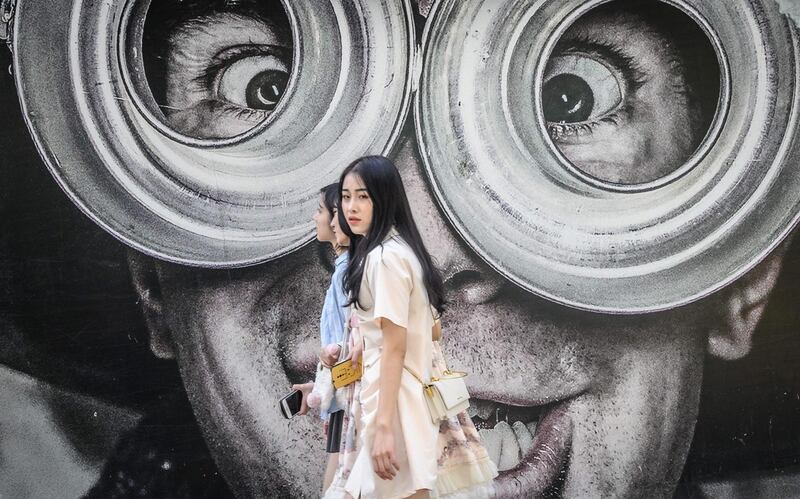 Young Thai women walk in front of a mural on a street in Bangkok. AFP