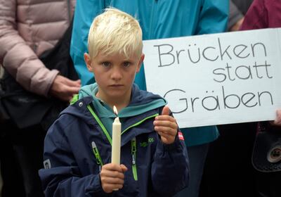 A boy holds candles as he stands in front of a poster reading 'bridges instead of cleavages' during a demonstration for democracy and against extremism in Chemnitz, eastern Germany, Sunday, Sept. 2, 2018. A week earlier a 35-year-old man had been killed in a stabbing sparking various protests. (AP Photo/Jens Meyer)