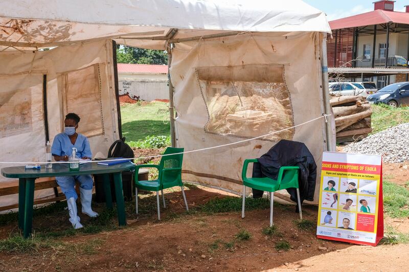 A medical attendant near a sign explaining to patients about the symptoms of Ebola at the entrance to Mubende Regional Referral Hospital. AP