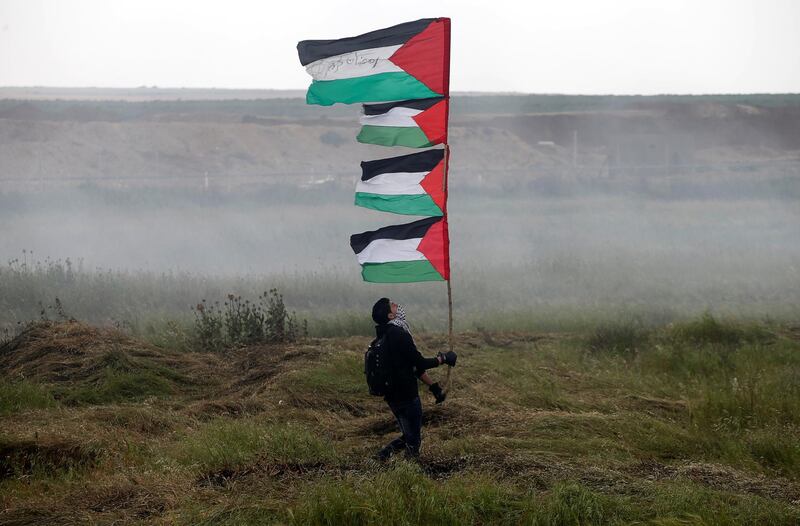 A demonstrator holds up Palestinian flags during clashes with Israeli troops along Israel's border with Gaza on March 30, 2018. Mohammed Salem / Reuters