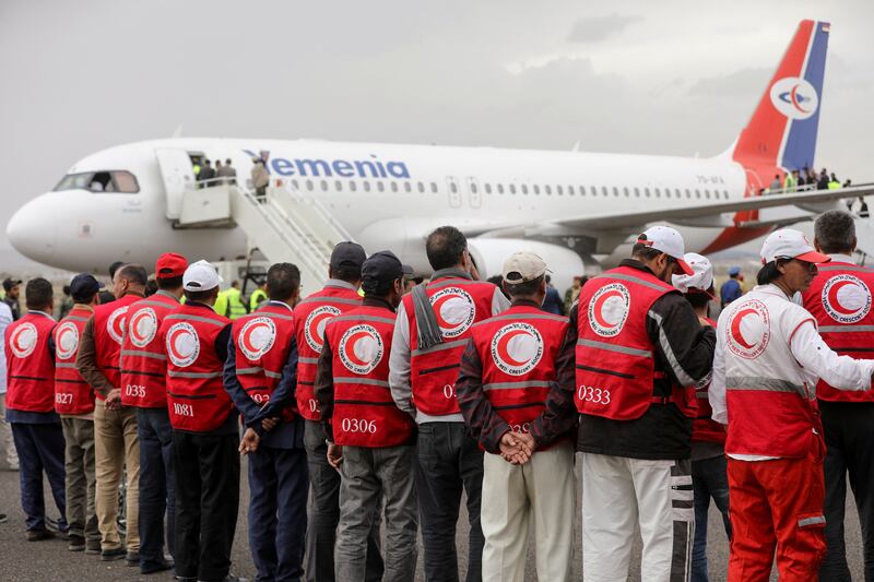 People wearing Yemen Red Crescent Society jackets wait as a plane carrying freed prisoners arrives at Sanaa Airport. Reuters