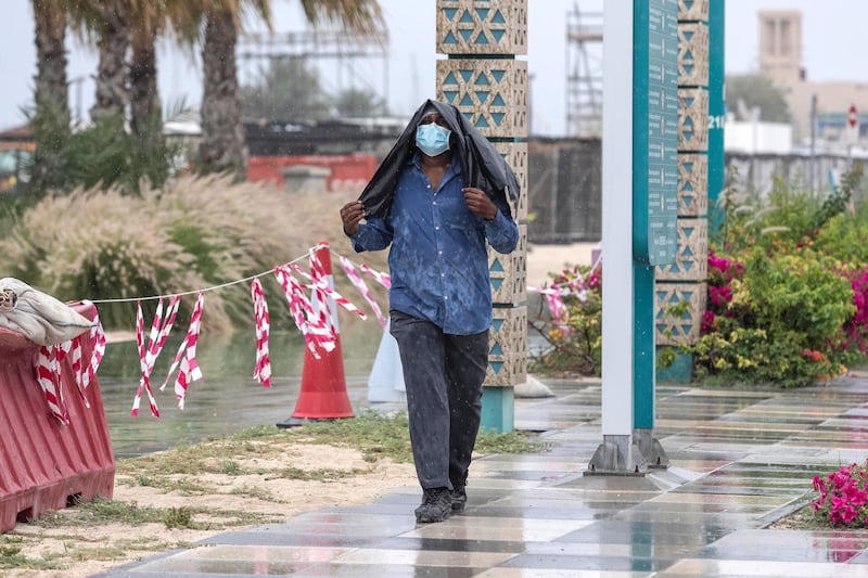 DUBAI, UNITED ARAB EMIRATES. 15 APRIL 2020. Rain pours down in Dubai. A man walks in the rain while covering himself in a platic sheet. (Photo: Antonie Robertson/The National) Journalist: STANDALONE. Section: National.
