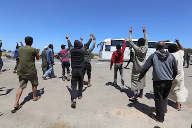 Libyan road transport workers stranded on the Tunisian-Libyan border crossing of Ras Jedir in southeastern Tunisia, gesture in farewell as a bus transporting repatriated Tunisian workers takes off, on April 21, 2020. Hundreds of Tunisians stranded for weeks in war-racked Libya due to the coronavirus have returned home after forcing their way through a border crossing, the UN and aid groups said, while Tunis's interior ministry denied that Tunisians had crossed the Ras Jedir border point a day earlier using force, saying authorities at the frontier allowed 652 to enter from Libya. / AFP / FATHI NASRI