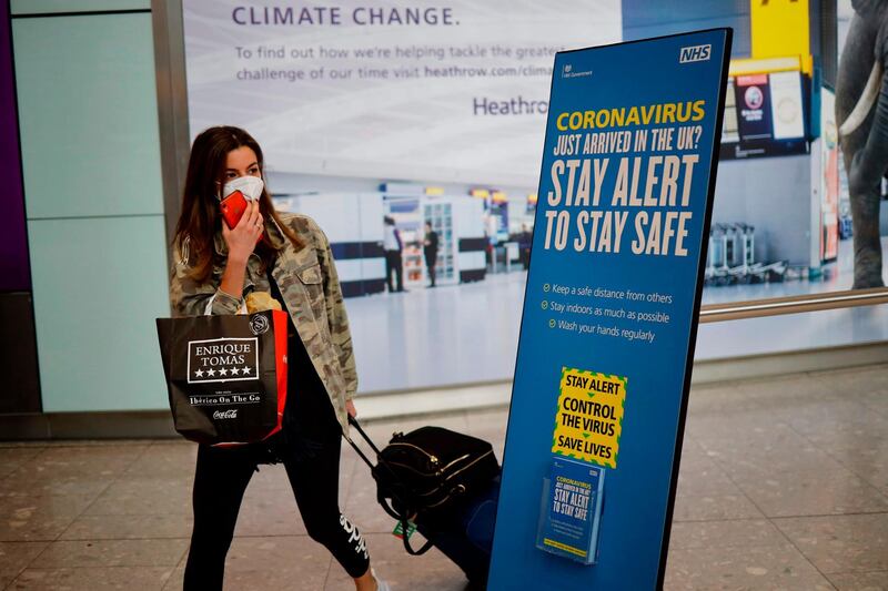 A newly arrived passenger wearing a face mask as a precaution against the novel coronavirus walks past a sign at Heathrow airport, west London, on May 22, 2020 with the British government's new 'Stay Alert' message on it. Travellers arriving in Britain will face 14 days in quarantine from next month to prevent a second coronavirus outbreak, the government announced on Friday, warning that anyone breaking the rules faced a fine or prosecution. / AFP / Tolga Akmen
