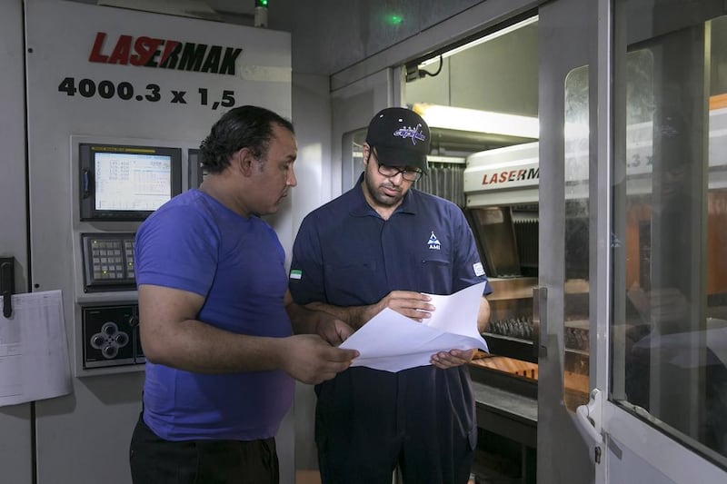 Ahmed Al Mazroei, left, works with Hassan Mohamed, programme operator of a laser-cutting machine at the 1,500-square-metre factory in Mussaffah. Silvia Razgova / The National