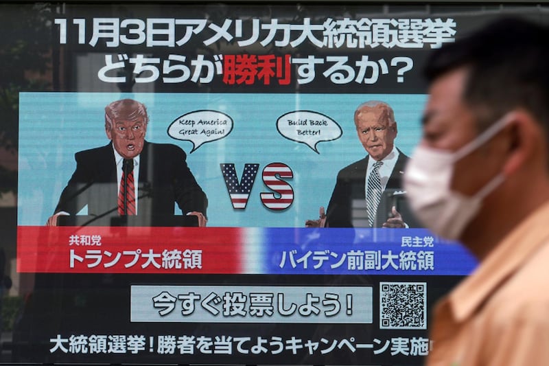 A man wearing a protective mask to help curb the spread of the coronavirus walks past a screen showing illustrations depicting Republican President Donald Trump, left, and Democratic candidate and former Vice President Joe Biden for an online voting to predict the winner in the Nov. 3 U.S. presidential election, in Tokyo Monday, Oct. 26, 2020. The Japanese letters at top read: "Which one will win in the Nov. 3 U.S. presidential election." (AP Photo/Eugene Hoshiko)