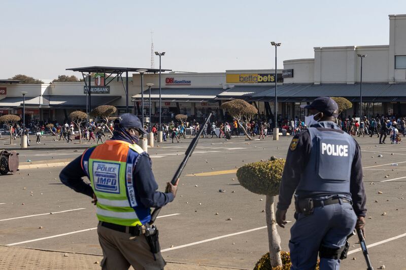 Saps members watch rioters looting the Jabulani Mall in Soweto.