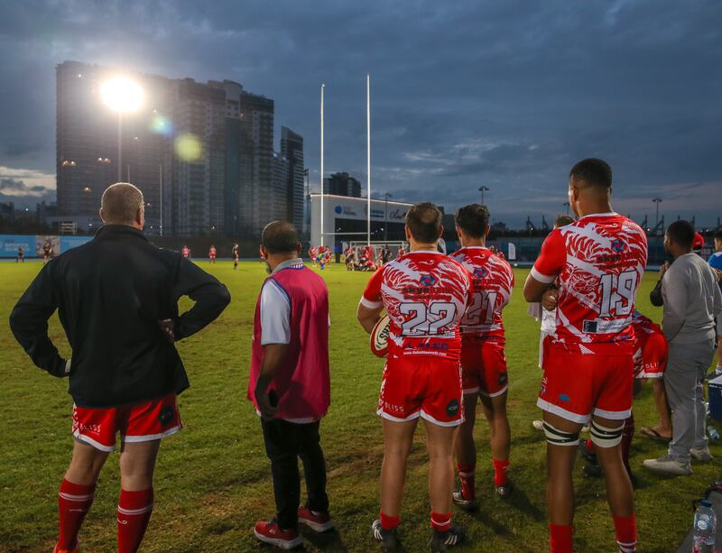 Dubai Tigers players and staff watch the game from the sidelines.