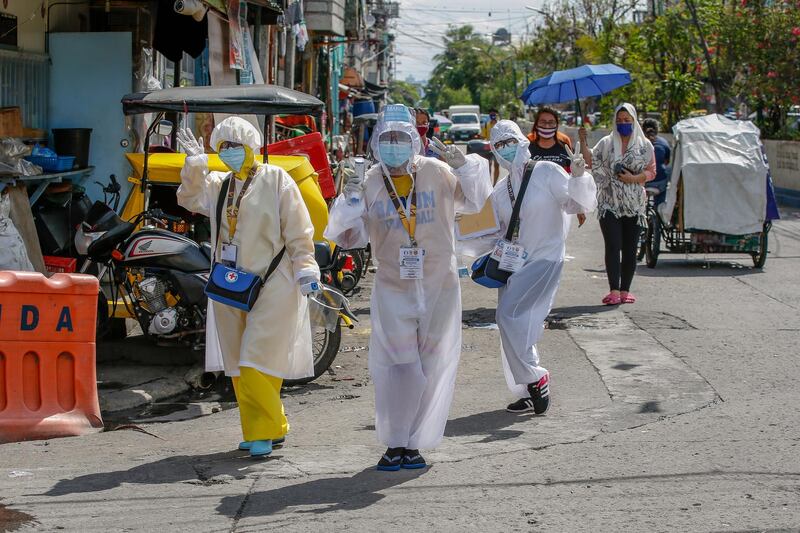 Healthcare workers in protective suits pose for pictures after visiting a house of a suspected Covid-19 case in Manila, Philippines, May 16. Mark R Cristino / EPA