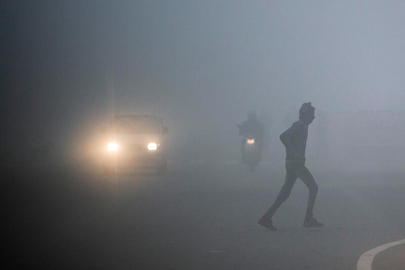 TOPSHOT - A man crosses a street as commuters make their way under heavy foggy conditions in New Delhi on December 30, 2019. / AFP / Jewel SAMAD
