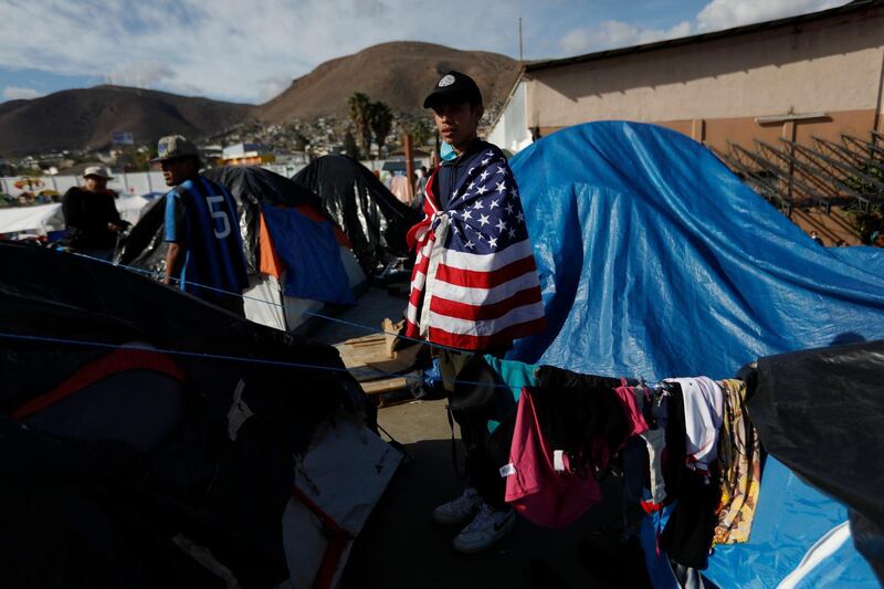 Daniel Castilla, 19, from Honduras, wears a US flag as he looks out over migrant tents at a former concert venue now serving as a shelter, in Tijuana, Mexico. AP Photo