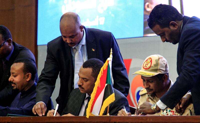 TOPSHOT - Sudan's protest leader Ahmad Rabie (C) and General Mohamed Hamdan Daglo "Hemeti" (R), deputy chief of the ruling Transitional Military Council (TMC) and commander of the Rapid Support Forces (RSF), sign documents during a ceremony to sign a "constitutional declaration" that paves the way for a Sudanese transition to civilian rule, in the capital Khartoum on August 17, 2019, accompanied by Ethiopian Prime Minister Abiy Ahmed (L). The agreement was signed by Mohamed Hamdan Daglo, deputy chief of the military council, and Ahmed al-Rabie, representing the Alliance for Freedom and Change protest umbrella group, an AFP reporter said. Heads of state, prime ministers and dignitaries from several countries attended the ceremony in Khartoum. / AFP / Ebrahim HAMID
