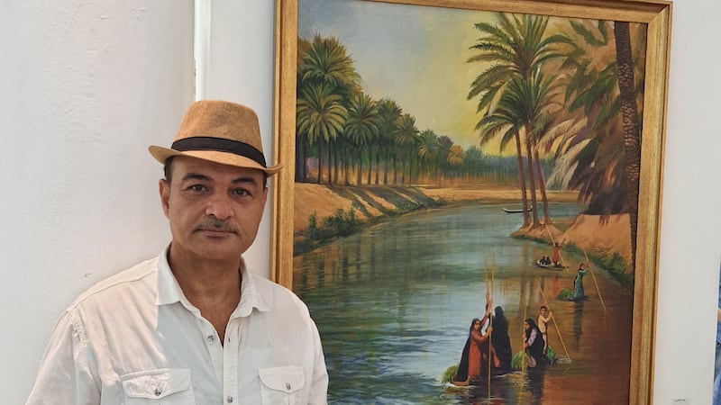 Artist Alaa Al Baldawi stands next to his painting that shows a scene from last century of an arable area in southern Iraq, where a tributary of the Tigris River is now almost gone. 