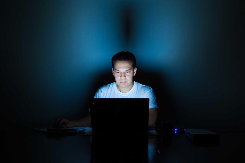 Portrait Of Young Man Using Laptop In Dark Room. Getty Images