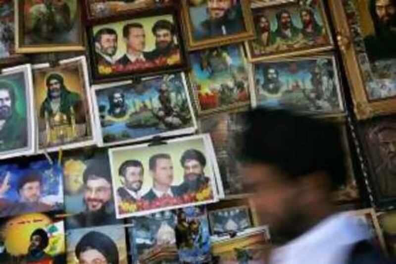 DAMASCUS, SYRIA, June 17 2006: An Iranian pilgrim walks past posters of Shiite religious figures and posters of Iranian President Mahmoud Ahmadinejad, Syrian President Bashar Al-Assad and Hezbollah Secretary General Sheikh Hassan Nassrallah, outside the Sayyida Zeinab Mosque.  Hundreds of Iranians visit the mosque each day. Shawn Baldwin/Corbis