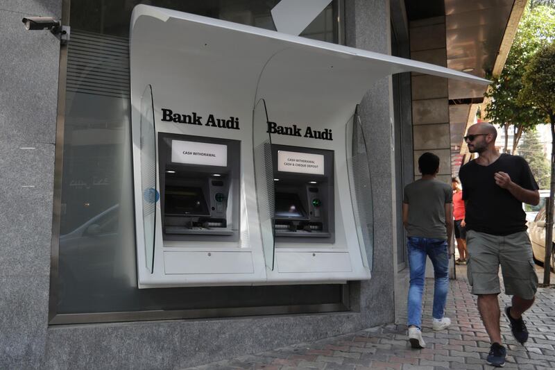 FILE - In this Tuesday, Nov. 12, 2019 file photo, people pass by an out of service ATM machines at a closed bank in the Lebanese capital Beirut. Lebanonâ€™s bank staff union announced Monday, Nov. 18, 2019 that itâ€™s ending a week-long strike after increased security and new regulations that make limits on withdrawal and dollar transfers official. The union said that banks will reopen Tuesday. (AP Photo/Hassan Ammar, File)