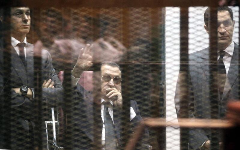 Former Egyptian President, Hosni Mubarak , flanked by his sons Gamal Mubarak, left, and brother Alaa Mubarak, waves from the defendants' cage during their trial at the Police Academy in Cairo. Hosni was sentenced to three years in prison in a retrial on charges of corruption.  EPA/KHALED ELFIQI